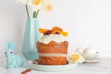 Paskalya pastası. Tavşan figürlü ve vazo narsisli. Beyaz fayans masasında, hafif grunge duvarının yanında.