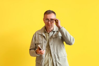 Sarı arka planda cep telefonu olan olgun bir adam. Son teslim tarihi kavramı