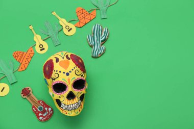 Meksika Ölüler Günü (El Dia de Muertos) için yeşil arka planda dekoratif kaktüs ve gitarlarla boyanmış insan kafatası.