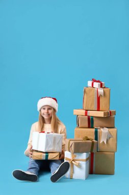 Mavi arka planda oturan Noel hediyeli küçük kız