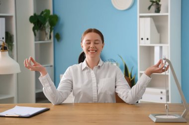 Genç iş kadını ofiste meditasyon yapıyor.