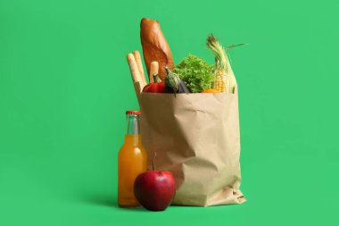 Yeşil zemin üzerinde farklı taze ürünler bulunan kağıt alışveriş torbası.