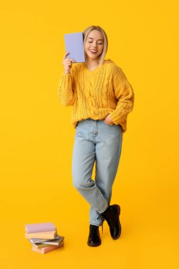 Sarı arka planda bir sürü kitabı olan güzel, genç ve mutlu bir kadın.