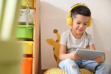 Evde tablet bilgisayar kullanan kulaklıklı küçük Asyalı çocuk.