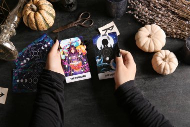 Koyu arkaplanda tarot kartları ve balkabakları olan bir cadı.