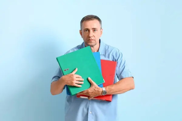 Stressed mature man with folders on blue background. Deadline concept