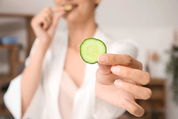 Young woman with cucumber slice on color background, closeup