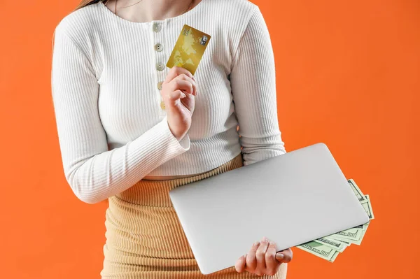 Young woman with credit card and laptop on orange background, closeup