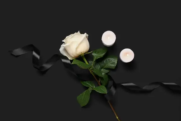 White rose with ribbon and burning candles on black background