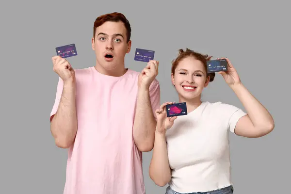 Young couple with credit cards on grey background