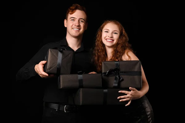 Young couple with gift boxes on dark background. Black Friday sale