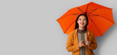 Gri arka planda şemsiyesi olan güzel, genç Asyalı bir kadın.