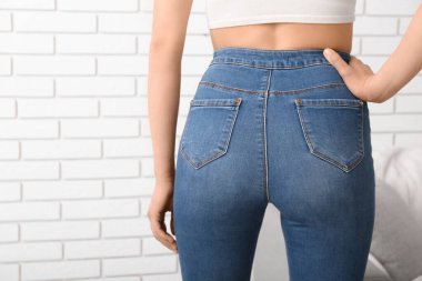 Açık tuğla duvarın yanında şık kotlu genç bir kadın.