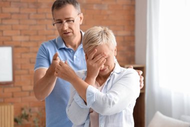 Ağlayan olgun bir kadın evde kocasına evlilik yüzüğü veriyor.