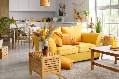 Açık uzay mutfağının içinde sarı kanepe ve ahşap sehpa var.