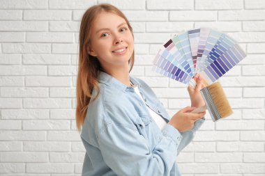 Renk örnekleri ve beyaz tuğla arka planı olan genç bir kadın.