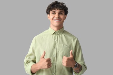 Gri arka planda baş parmak gösteren yakışıklı bir genç portresi.