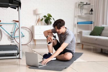 Evde su ve dizüstü bilgisayarı olan genç bir adam. Çevrimiçi eğitim kavramı