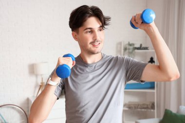 Sportif genç adam evde dambıllarla egzersiz yapıyor.