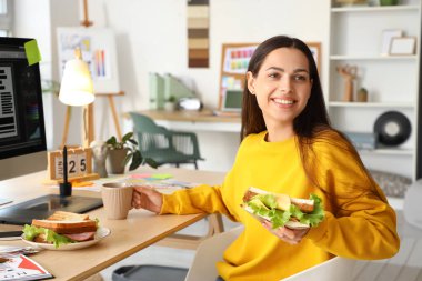Ofisinde lezzetli sandviçli ve kahveli genç bir kadın var.