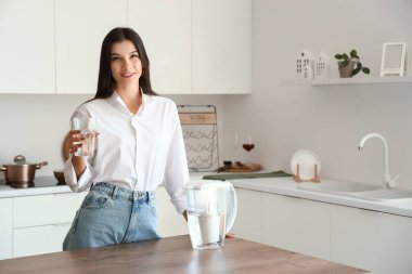 Mutfakta cam ve su filtresi olan genç bir kadın.