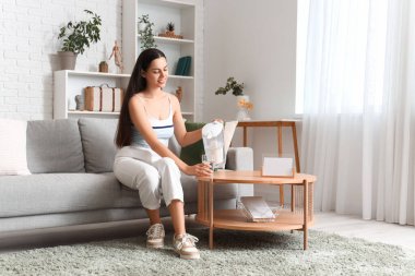 Oturma odasındaki kanepede oturan ve filtre sürahisinden cam bardağa saf su döken güzel genç bir kadın.