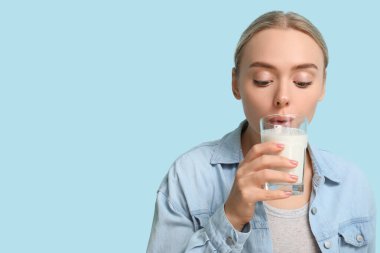 Güzel genç bayan mavi arka planda süt içiyor.