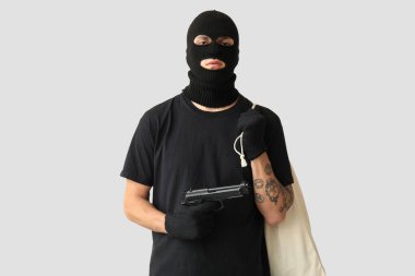 Gri arka planda silahlı ve çantalı bir erkek hırsız.