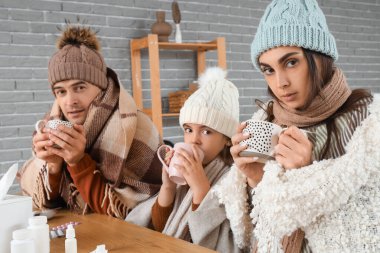 Sıcak giysili bir aile evde ısıtma olmadan çay içiyor.