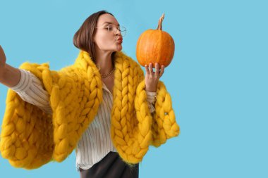 Ekose ve balkabaklı güzel bir kadın mavi arka planda selfie çekiyor.