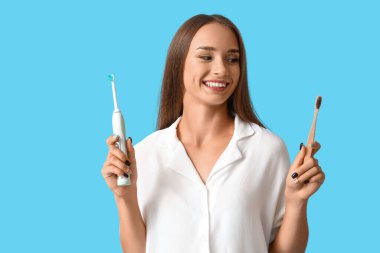 Mavi arka planda diş fırçası olan gülümseyen genç bir kadın.