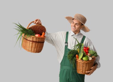Açık arkaplanda sepetler dolusu sebze taşıyan erkek çiftçi.