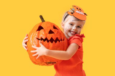 Cadılar Bayramı için giyinmiş küçük kız, sarı arka planda balkabağı.