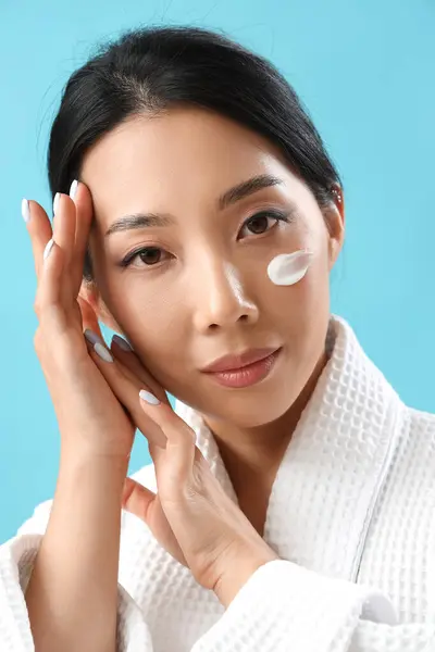Beautiful Asian woman with cream on her face against blue background