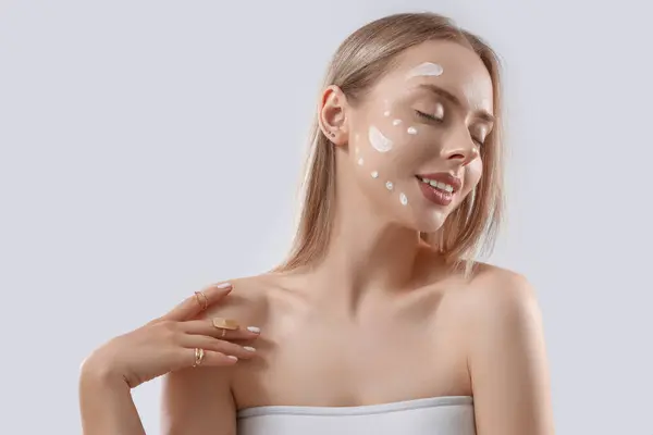 Sexy young woman with cream on her face against light background