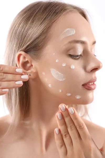 Sexy young woman with cream on her face against white background