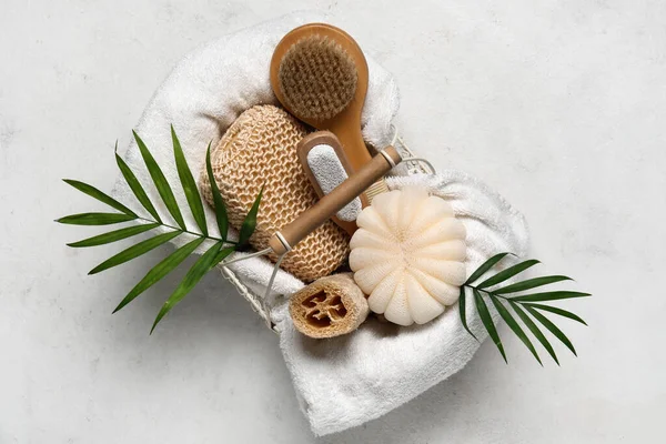 Basket with different bath supplies and palm leaves on light background