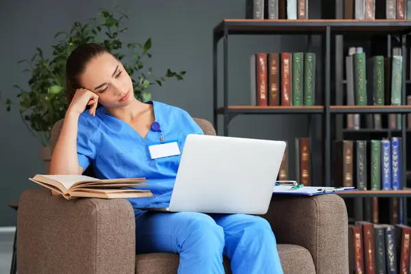 Tired female medical student studying with laptop in library