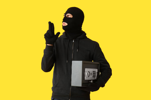 Мужчина-вор с сейфом показывает жест пистолета на желтом фоне