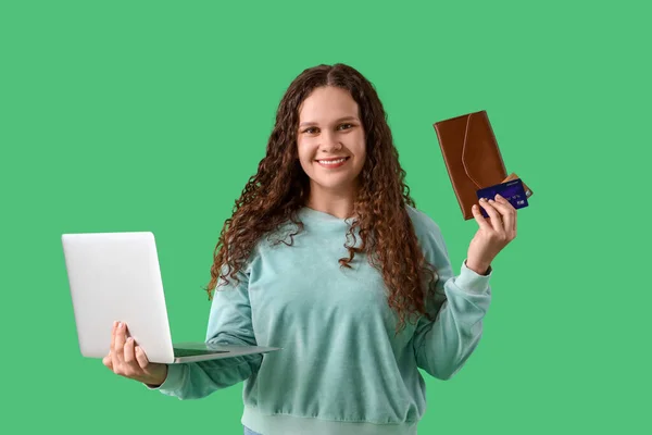 Young woman with laptop, wallet and credit cards shopping online on green background