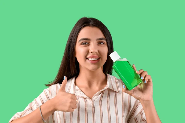 Smiling young woman with mouth rinse showing thumb-up on green background