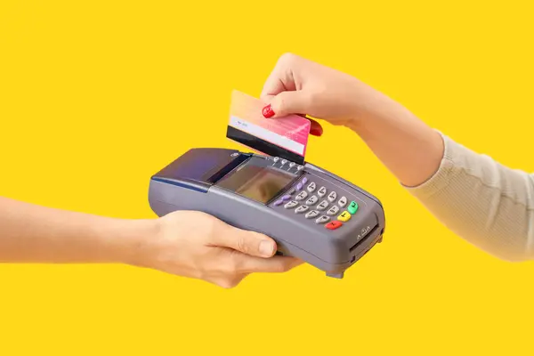Woman with credit card paying via terminal on yellow background, closeup