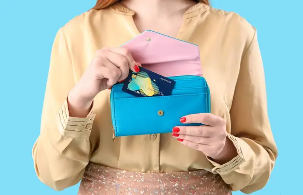 Young woman with credit card and wallet on blue background, closeup