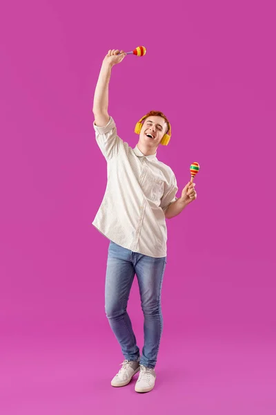 Young man in headphones with Mexican maracas on purple background