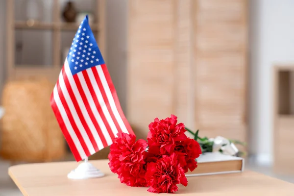 USA flag with carnation flowers on table in room, closeup. Veterans Day celebration
