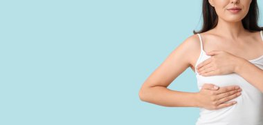 Genç bir kadın açık mavi arka planda göğsünü kontrol ediyor, mesaj için yer var mı diye.