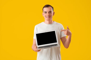 Genç adam sarı arka planda dizüstü bilgisayara bakıyor.