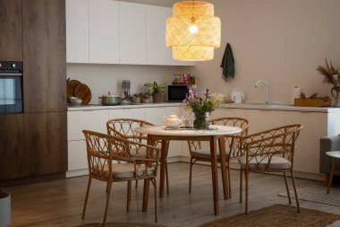 Modern mutfağın içinde, yemek masasında parlayan lamba ve vazo var.