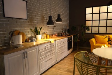 Parlayan lambaları, yemek masası, sarı kanepesi ve akşamları beyaz tezgahı olan modern mutfağın içi.