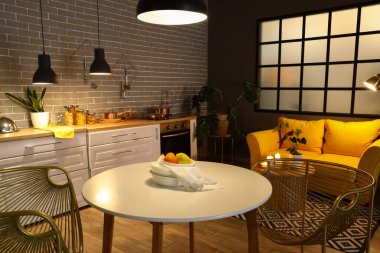 Parlayan lambaları, yemek masası, sarı kanepesi ve akşamları beyaz tezgahı olan modern mutfağın içi.